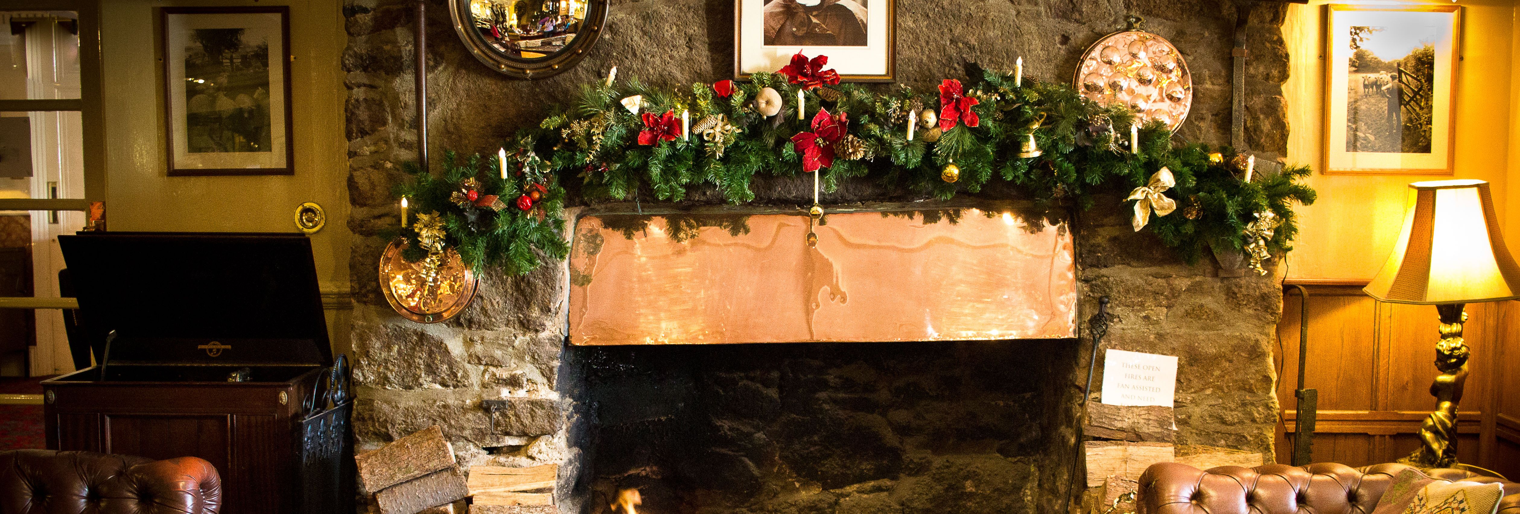 Cozy living room with a stone fireplace decorated for Christmas, featuring a copper mantel, festive garland, and vintage furniture.