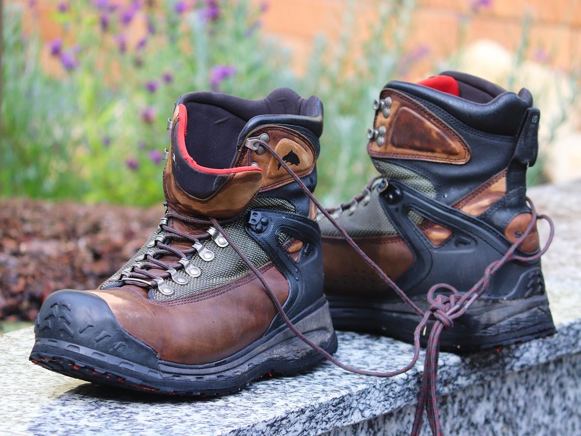 Pair of rugged brown hiking boots with laces, placed outdoors on a stone surface.