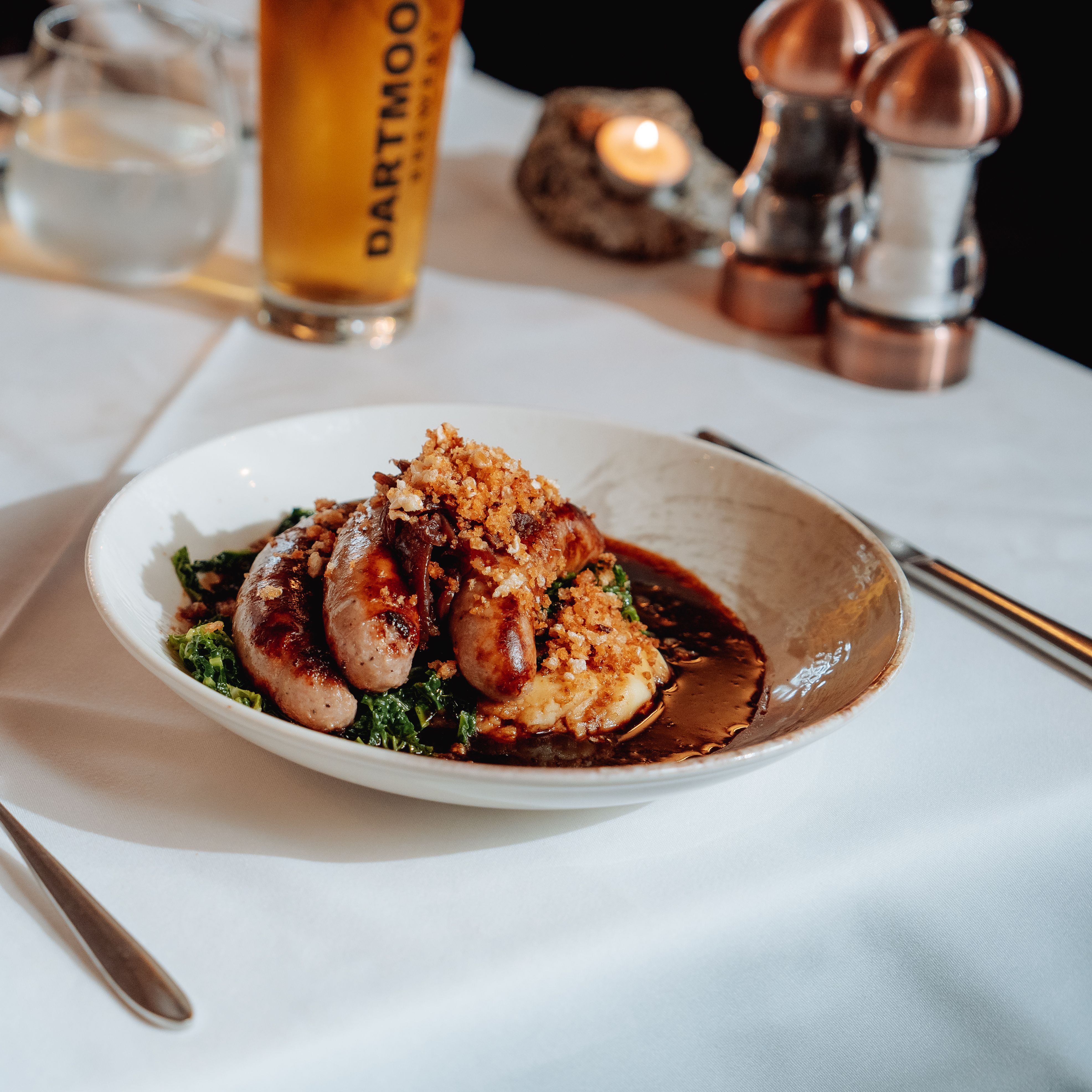 Plate of sausages and mashed potatoes served with a pint of Dartmoor Jail Ale on a restaurant table.