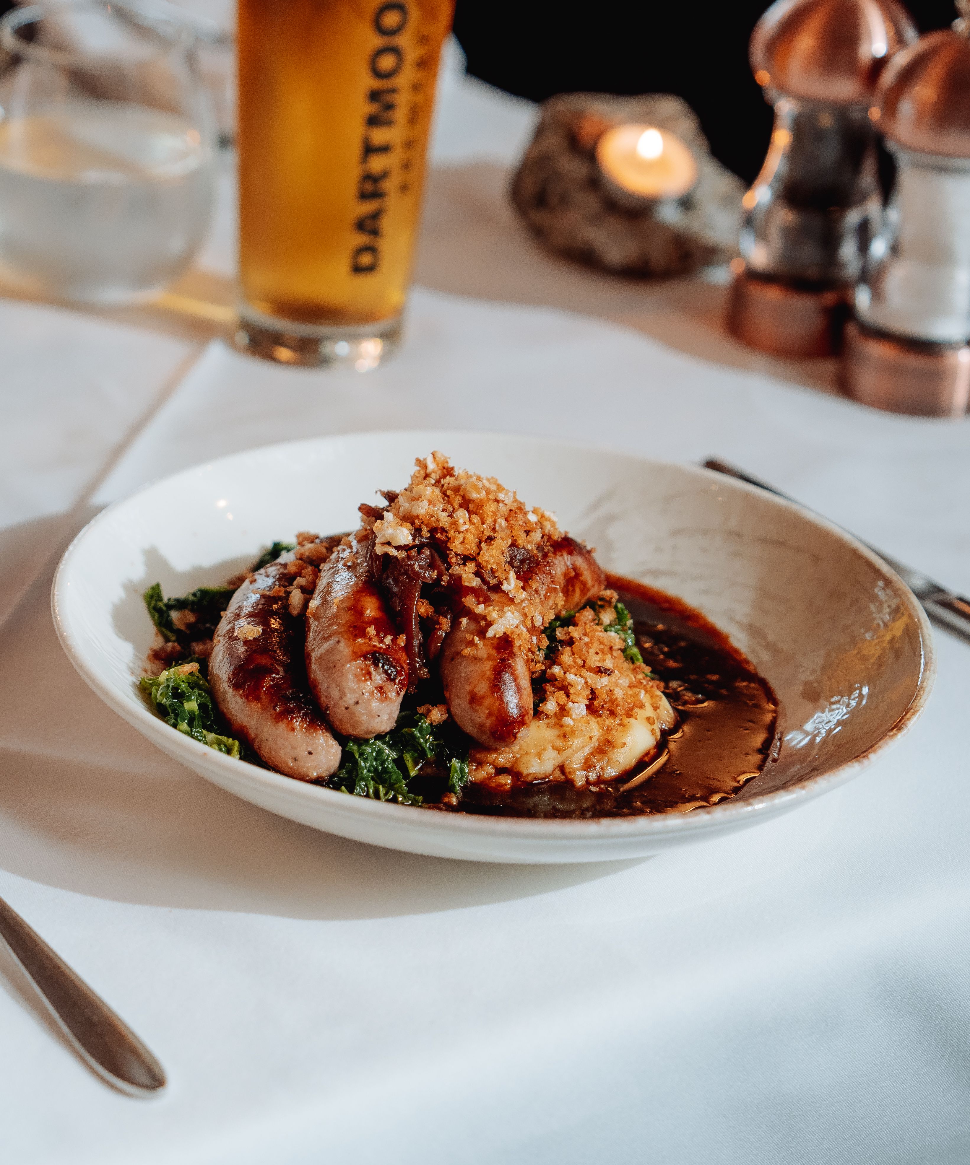 Plate of sausages and mashed potatoes served with a pint of Dartmoor Jail Ale on a restaurant table.
