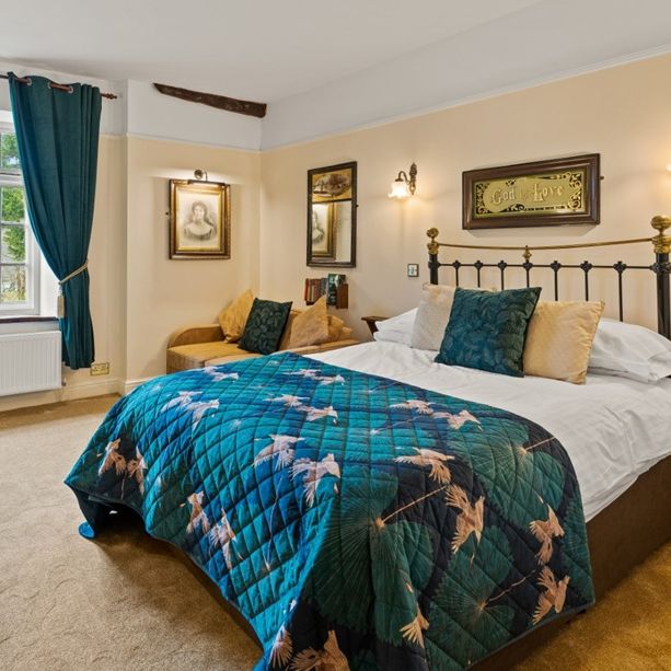 Cozy country-style double bedroom with teal quilt, vintage decor, and a large window with curtains.