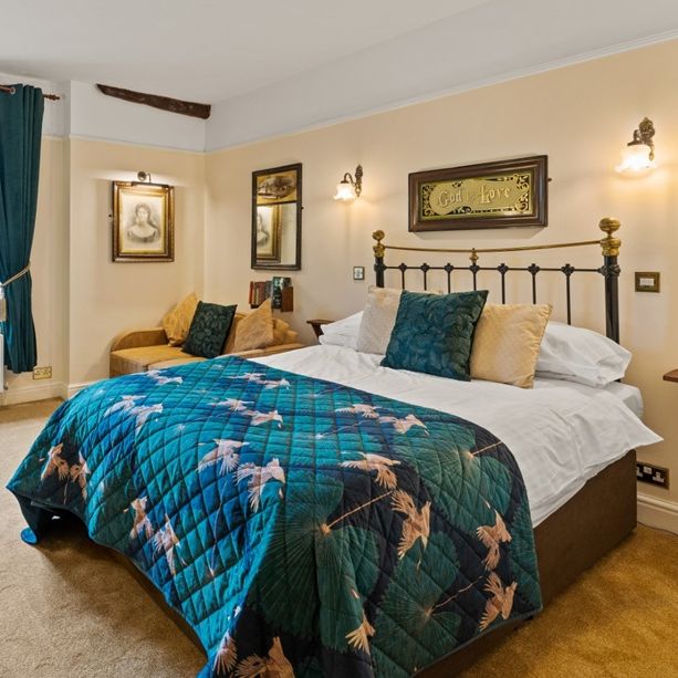 Cozy country-style double bedroom with teal quilt, vintage decor, and a large window with curtains.