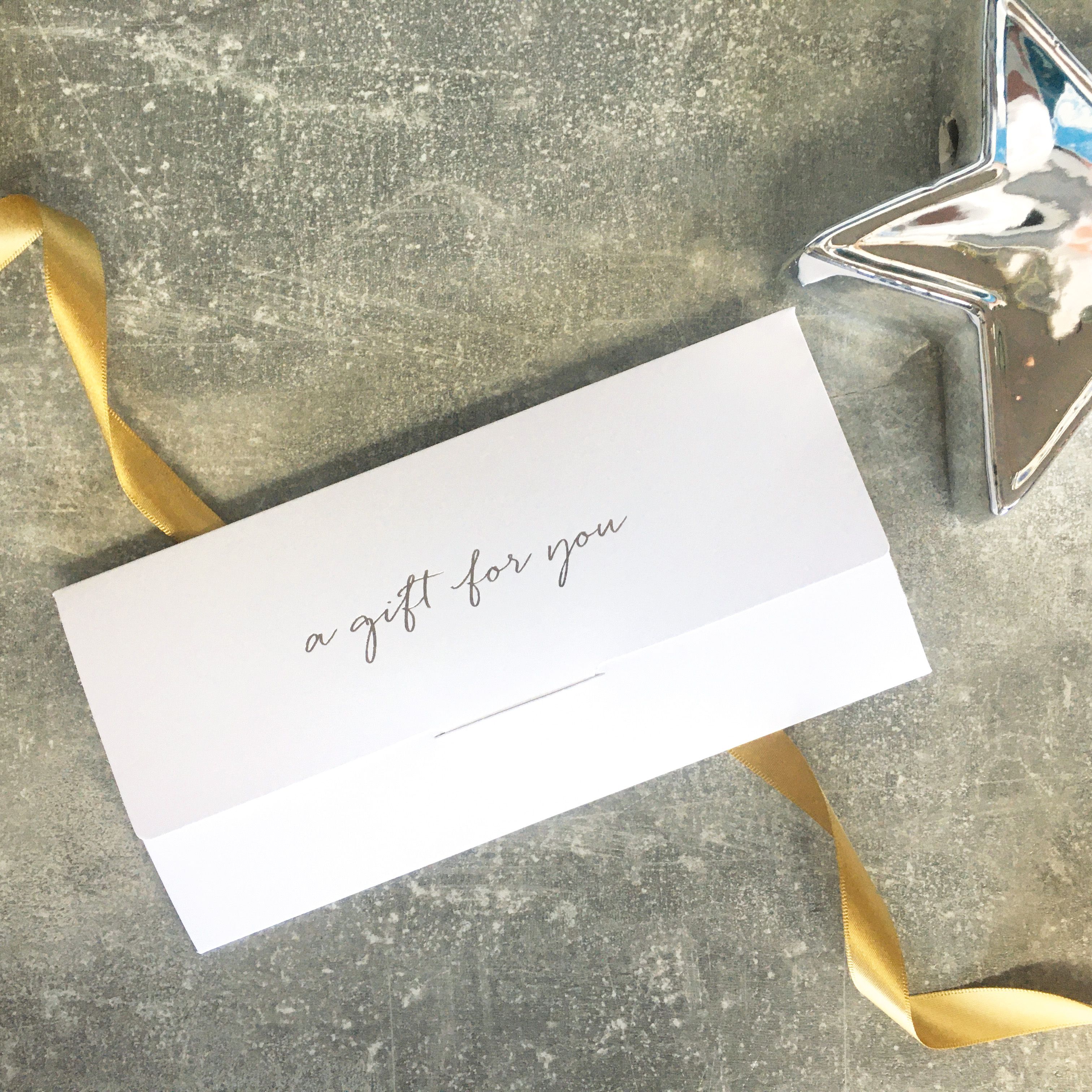 White gift voucher envelope with 'a gift for you' written on it, next to a gold ribbon and a silver star ornament.