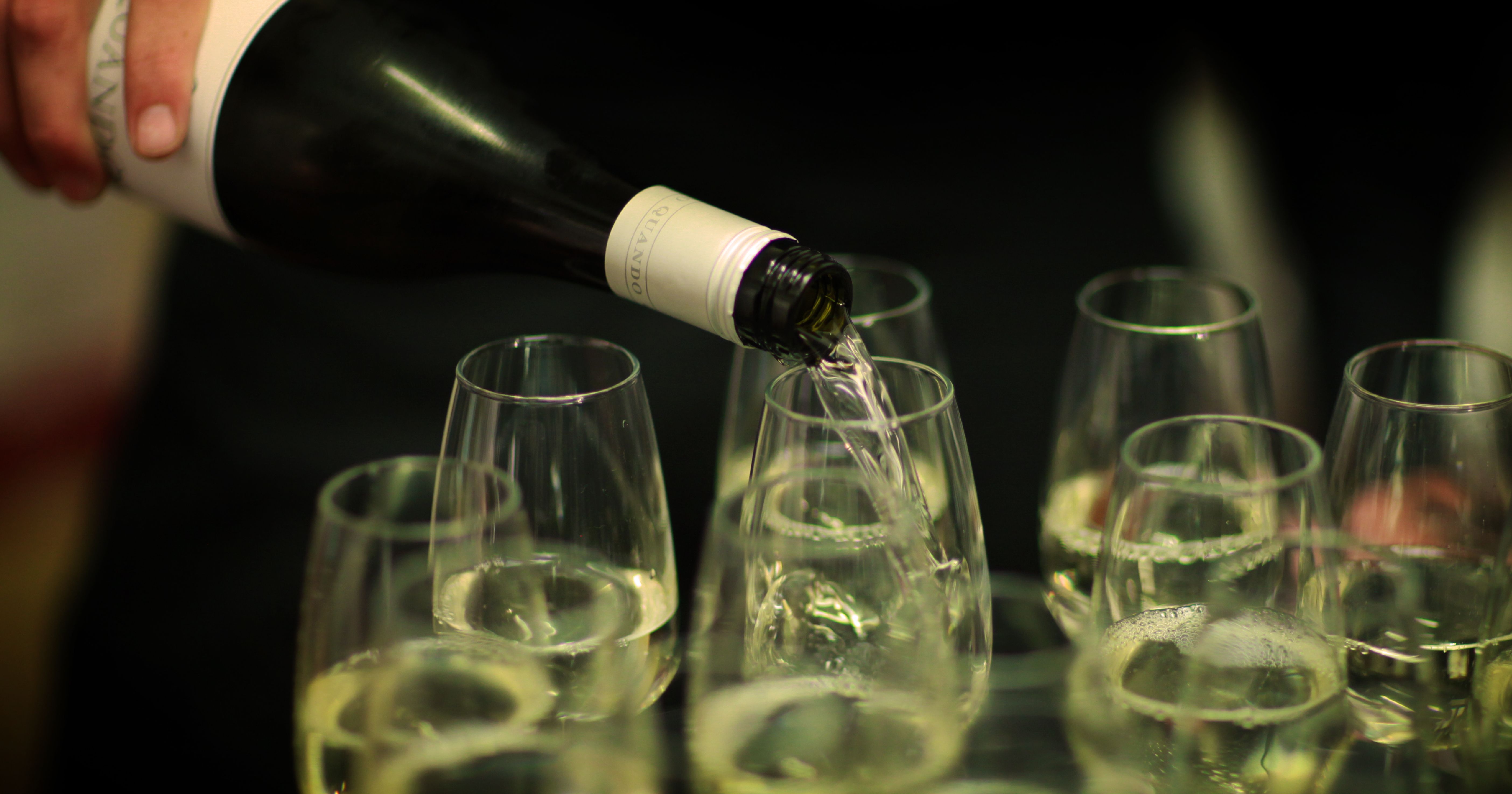 Person pouring white wine into several glasses
