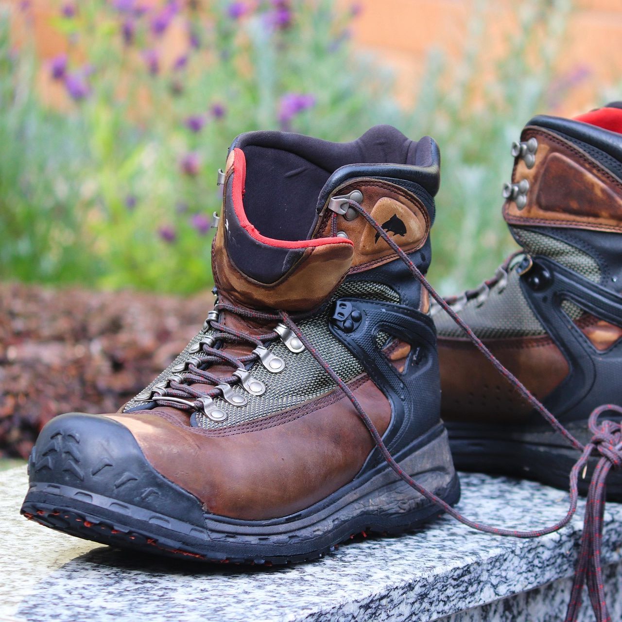 A pair of rugged brown and black hiking boots with laces, placed outdoors on a stone surface.