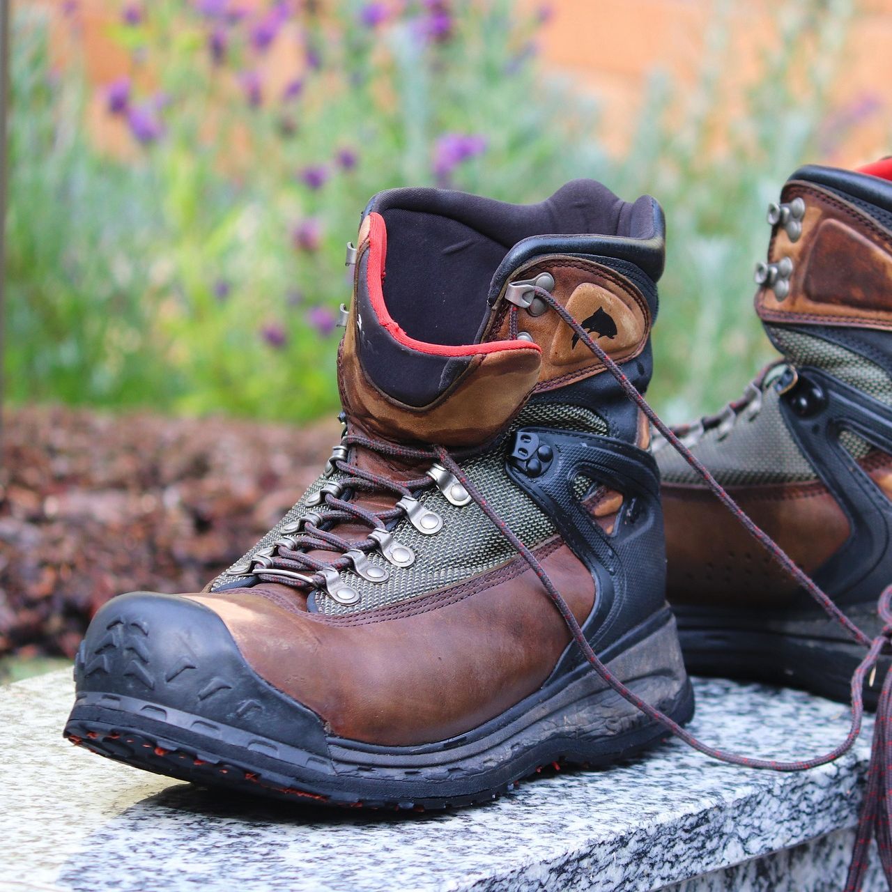 A pair of rugged brown and black hiking boots with laces, placed outdoors on a stone surface.