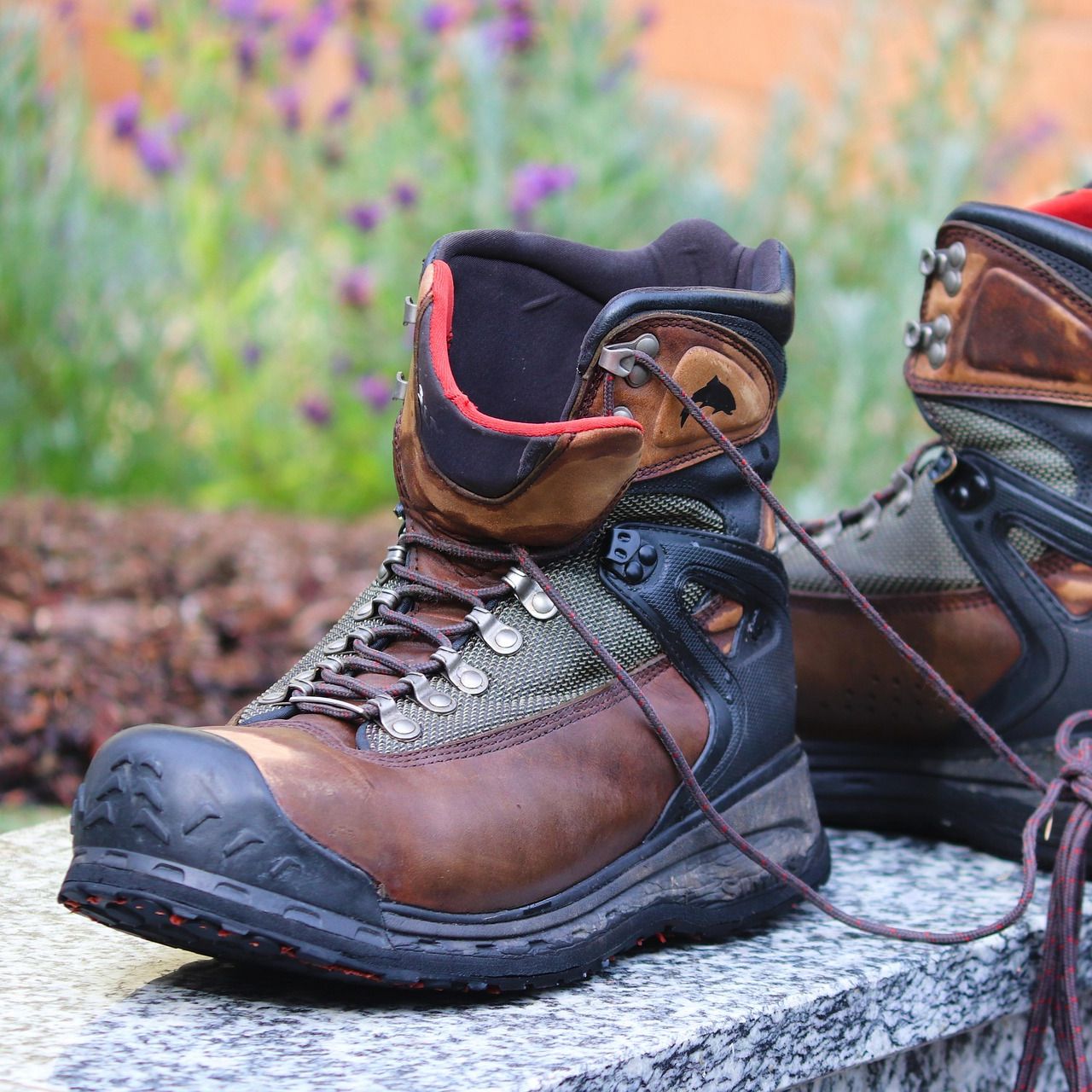 A pair of rugged brown and black hiking boots with laces, placed outdoors on a stone surface.