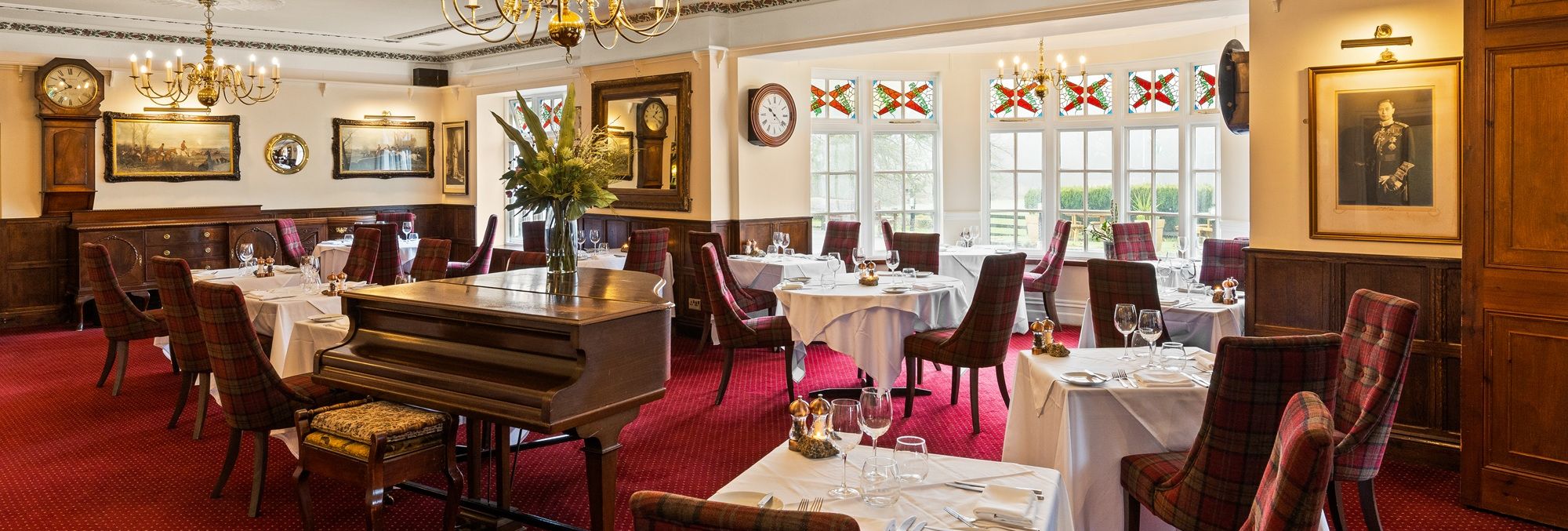 Elegant restaurant dining room with red plaid chairs, white tablecloths, chandeliers, and a grand piano.