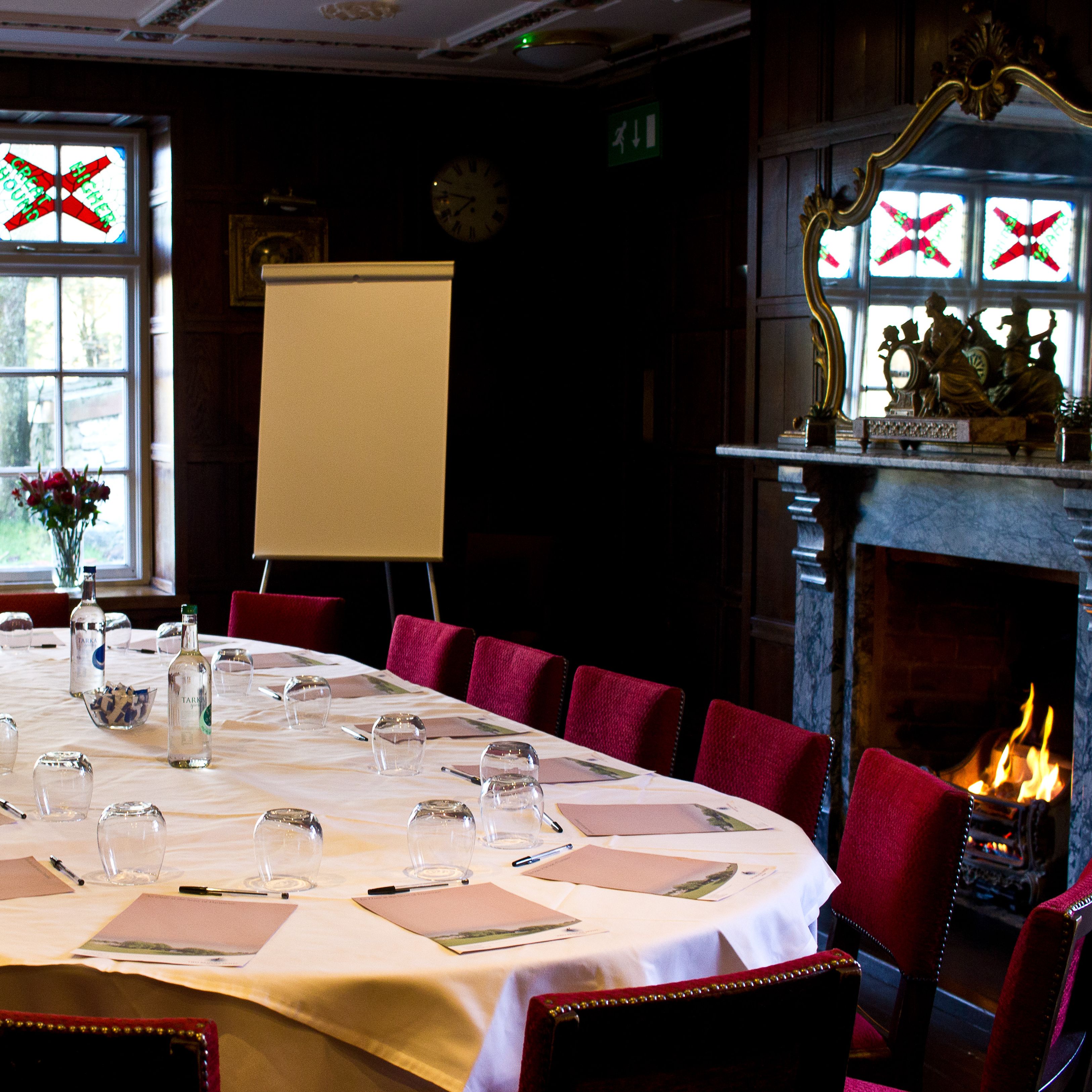 Elegant meeting room with an oval table, red chairs, a fireplace, and stained glass windows.
