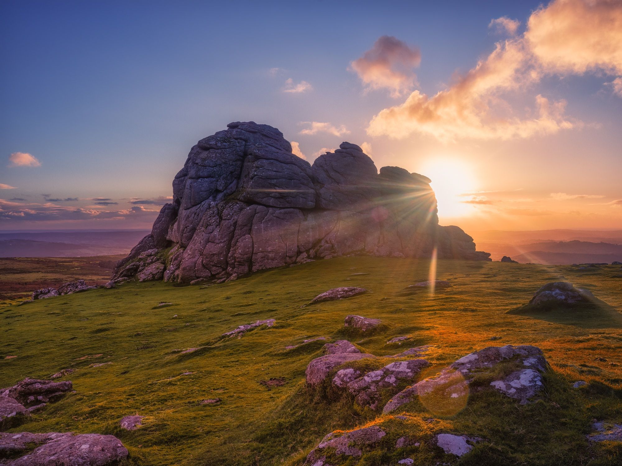 Rocky tor on Dartmoor at sunset with sun rays and grassy foreground