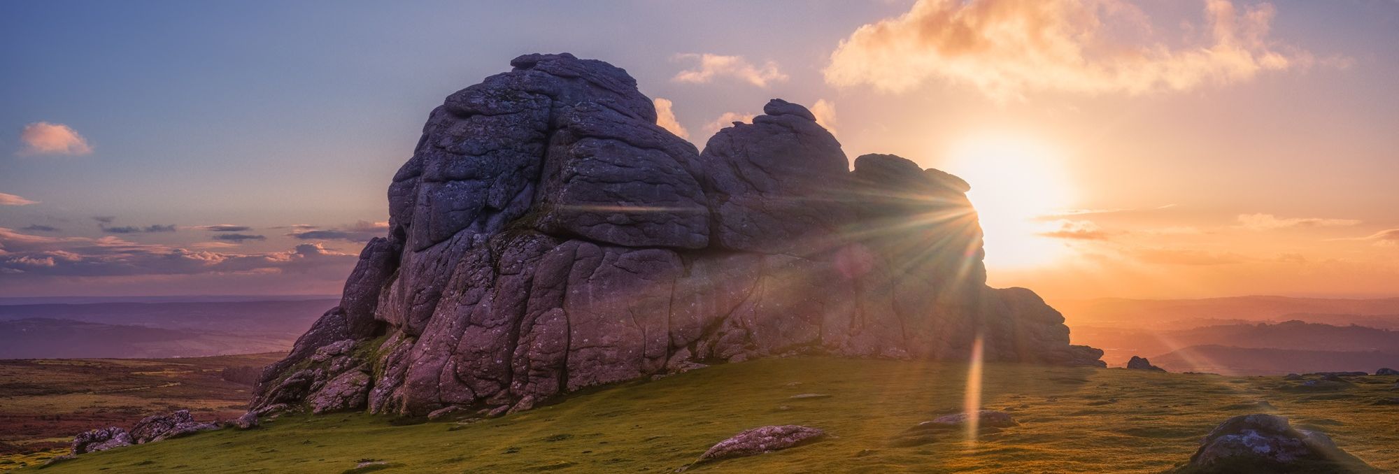 Rocky tor on Dartmoor at sunset with sun rays and grassy foreground