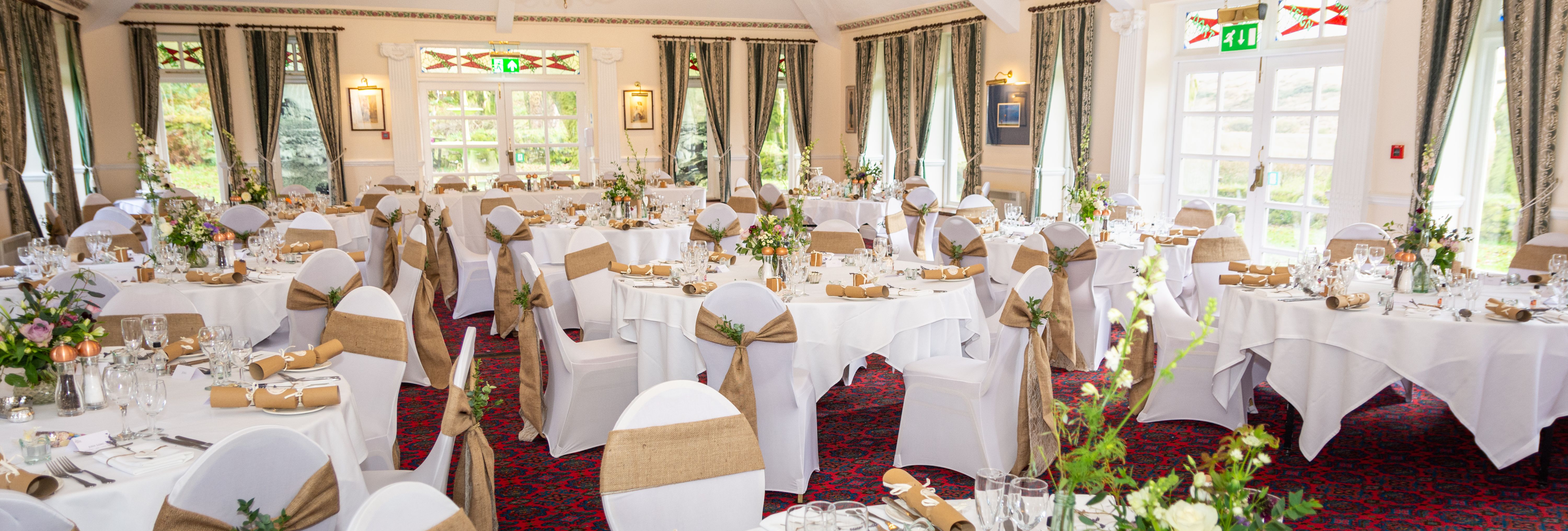 Elegant wedding reception room with round tables dressed in white cloth, rustic chair sashes, and floral centerpieces.