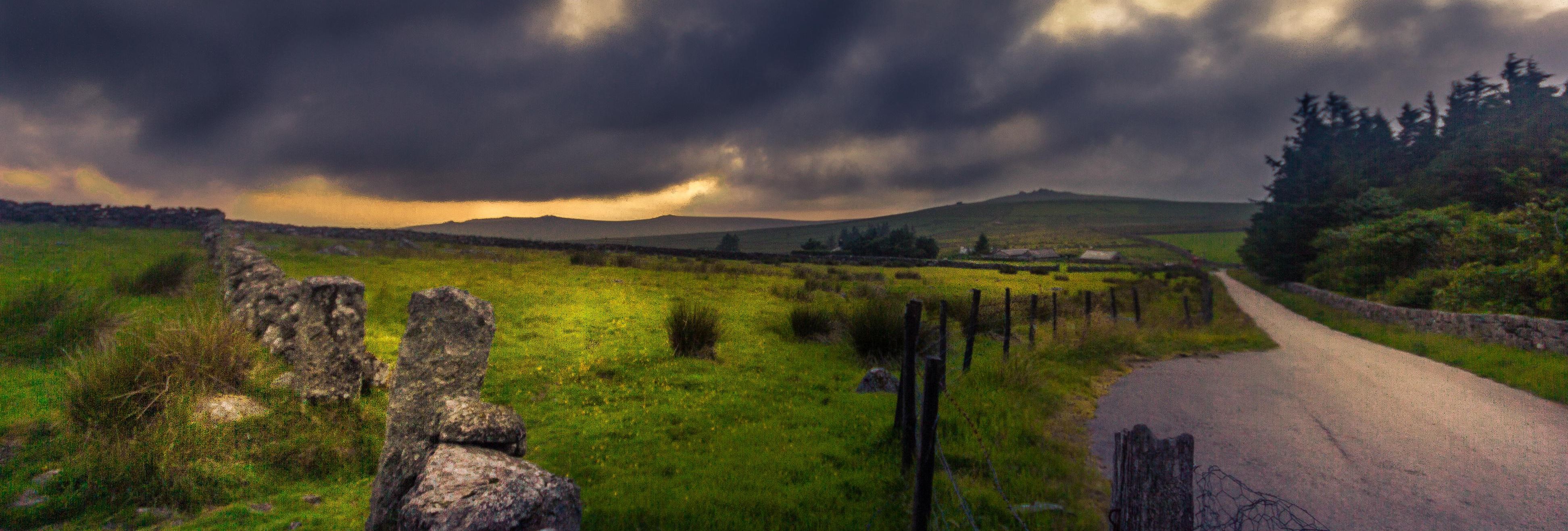 Dramatic dark clouds over a rural countryside road and green fields