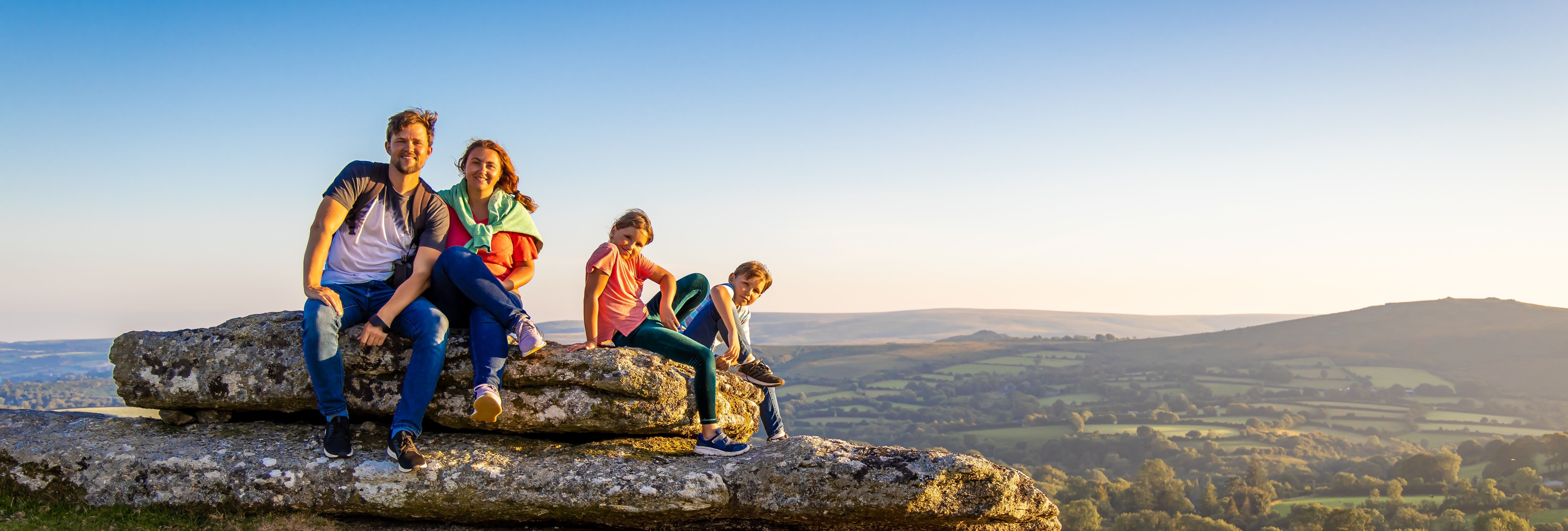Family sitting on large rocks in Dartmoor National Park with rolling hills in the background