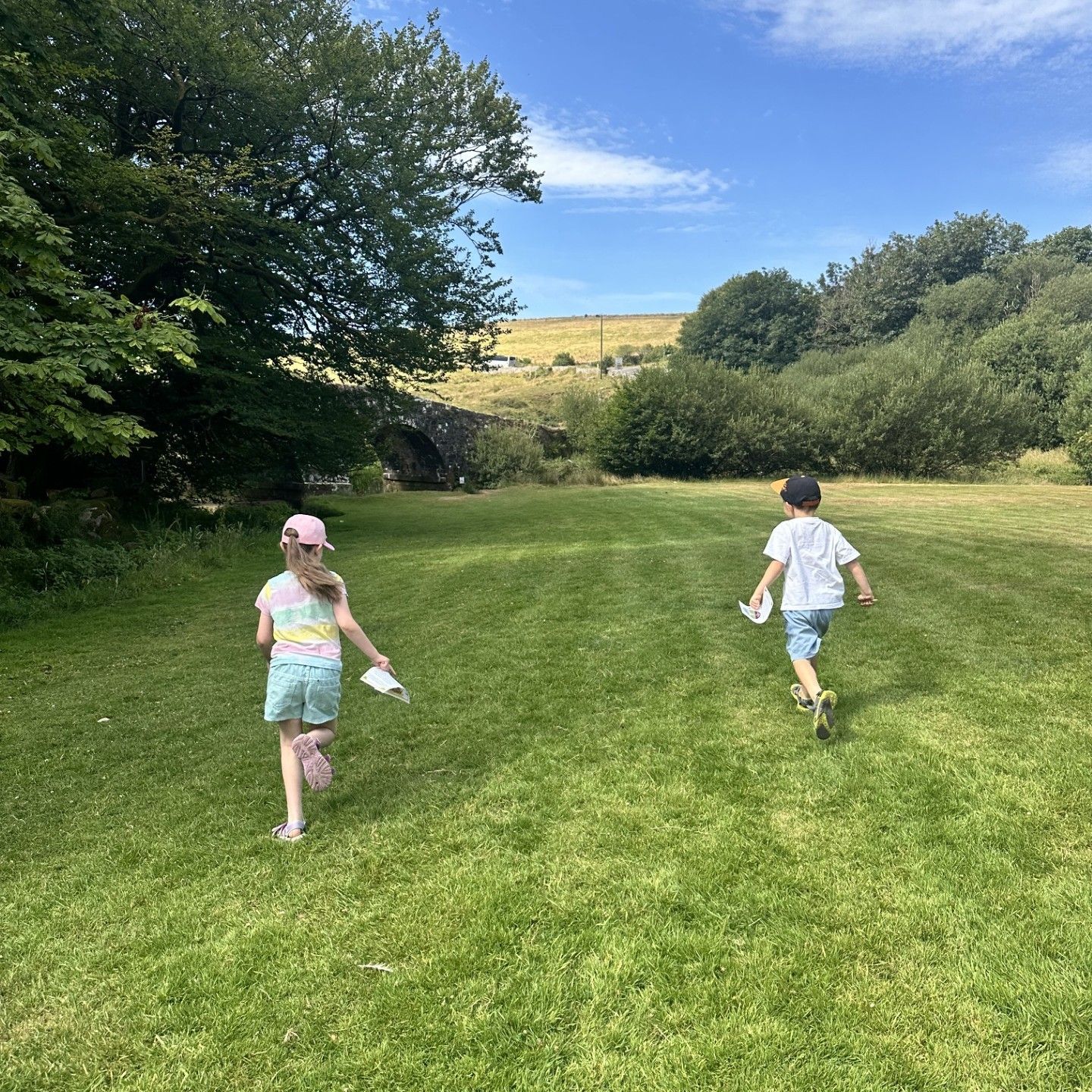 Two children running on a grassy field under a blue sky