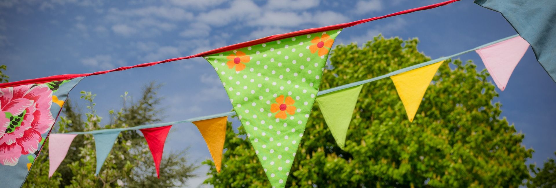 Colorful bunting flags hanging outdoors with trees and blue sky in the background