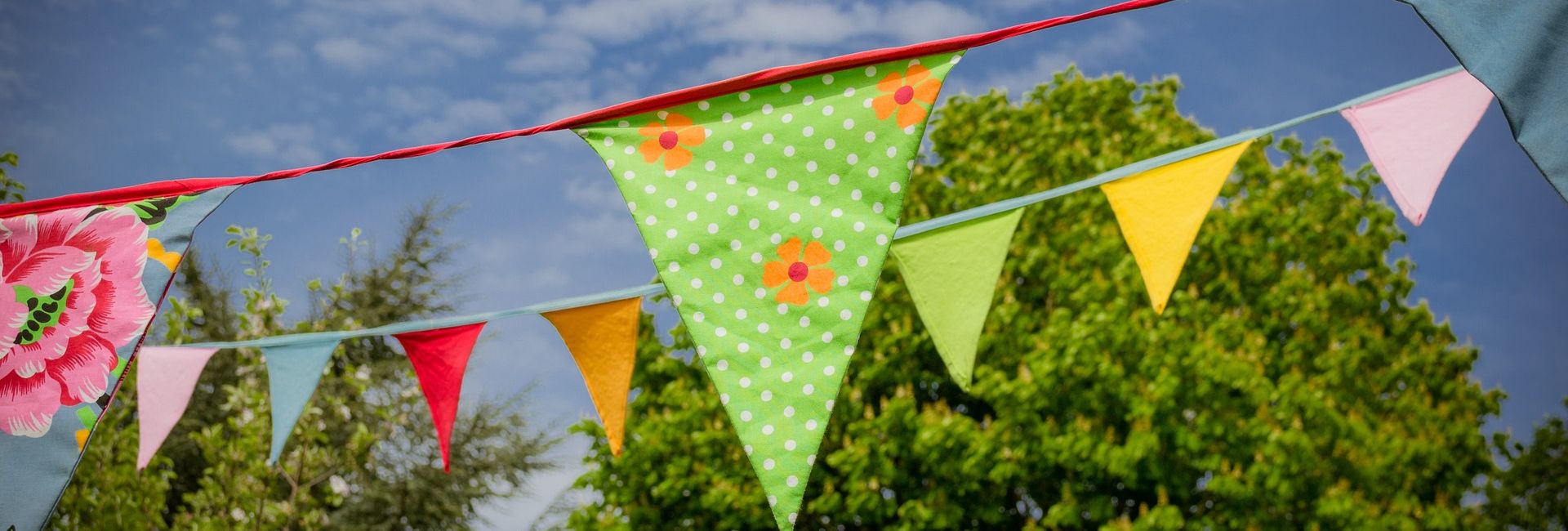 Colorful bunting flags hanging outdoors with trees and blue sky in the background