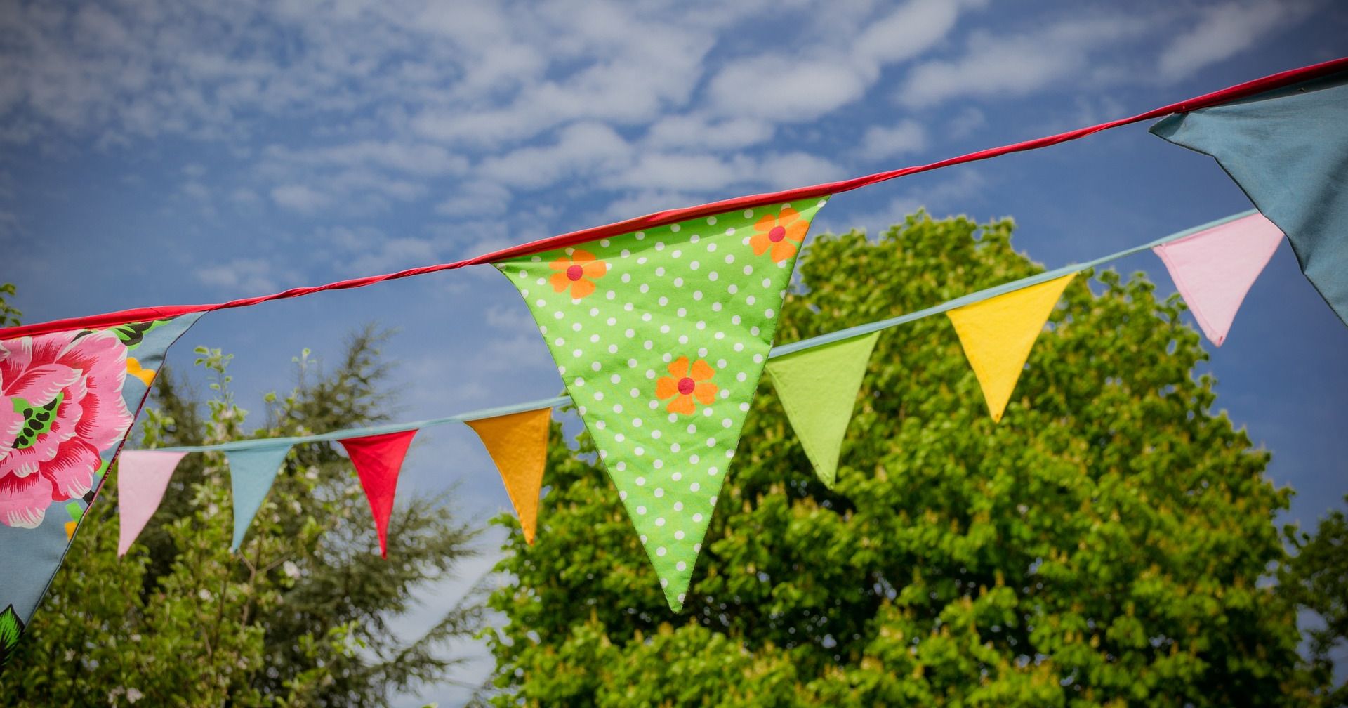 Colorful bunting flags hanging outdoors with trees and blue sky in the background