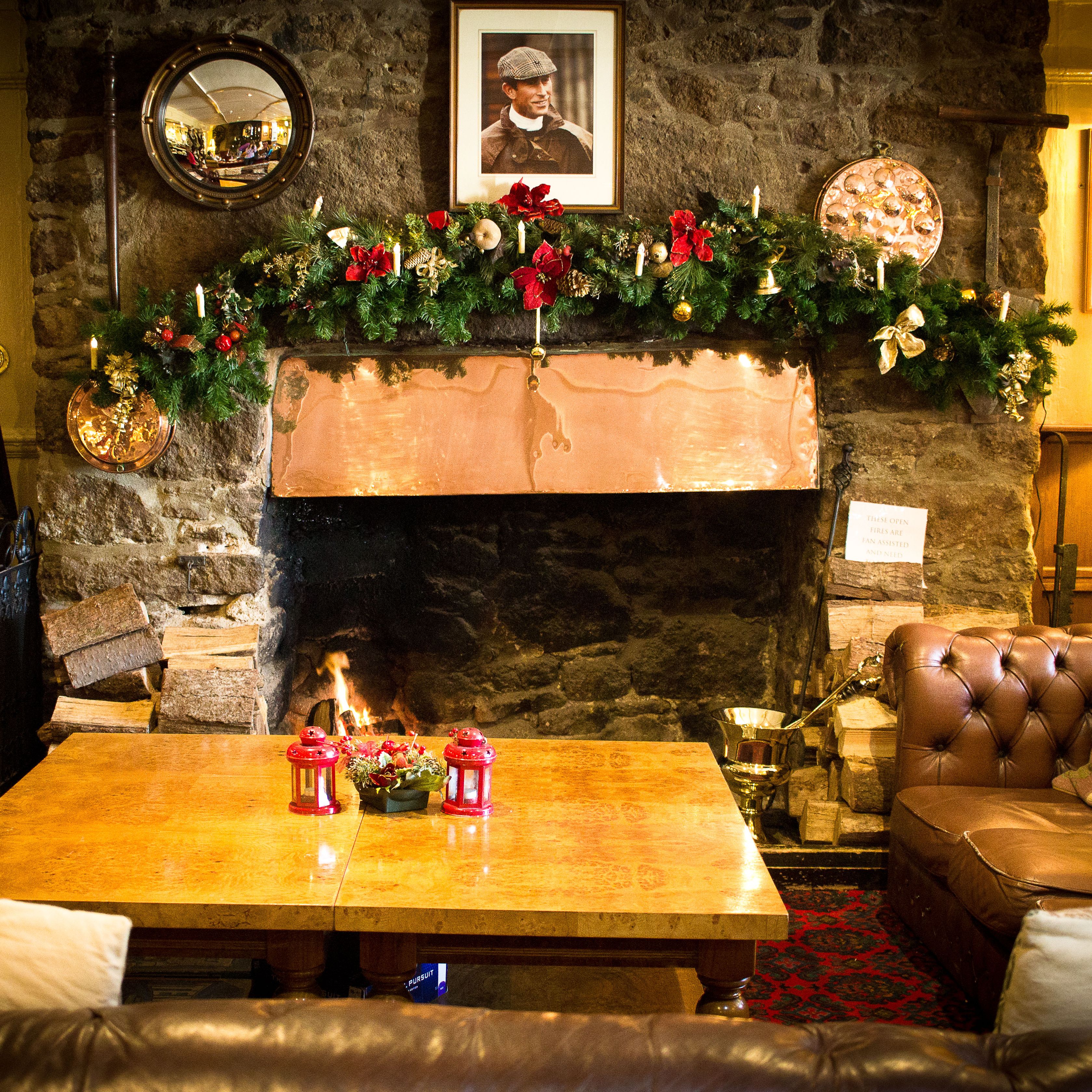 Cozy living room with a decorated stone fireplace, leather sofas, a wooden coffee table, and festive holiday garland