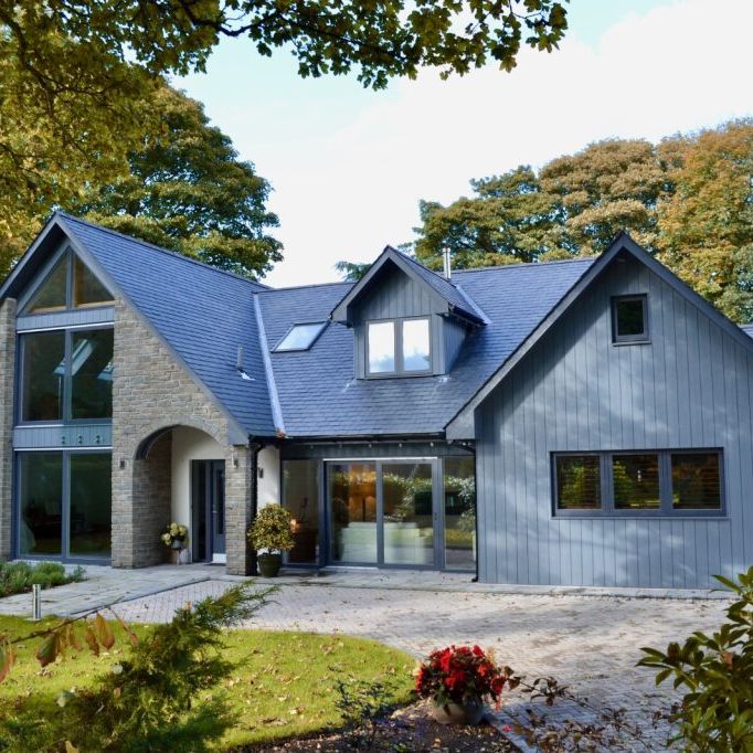 Modern house with stone and wood exterior surrounded by trees and a landscaped garden