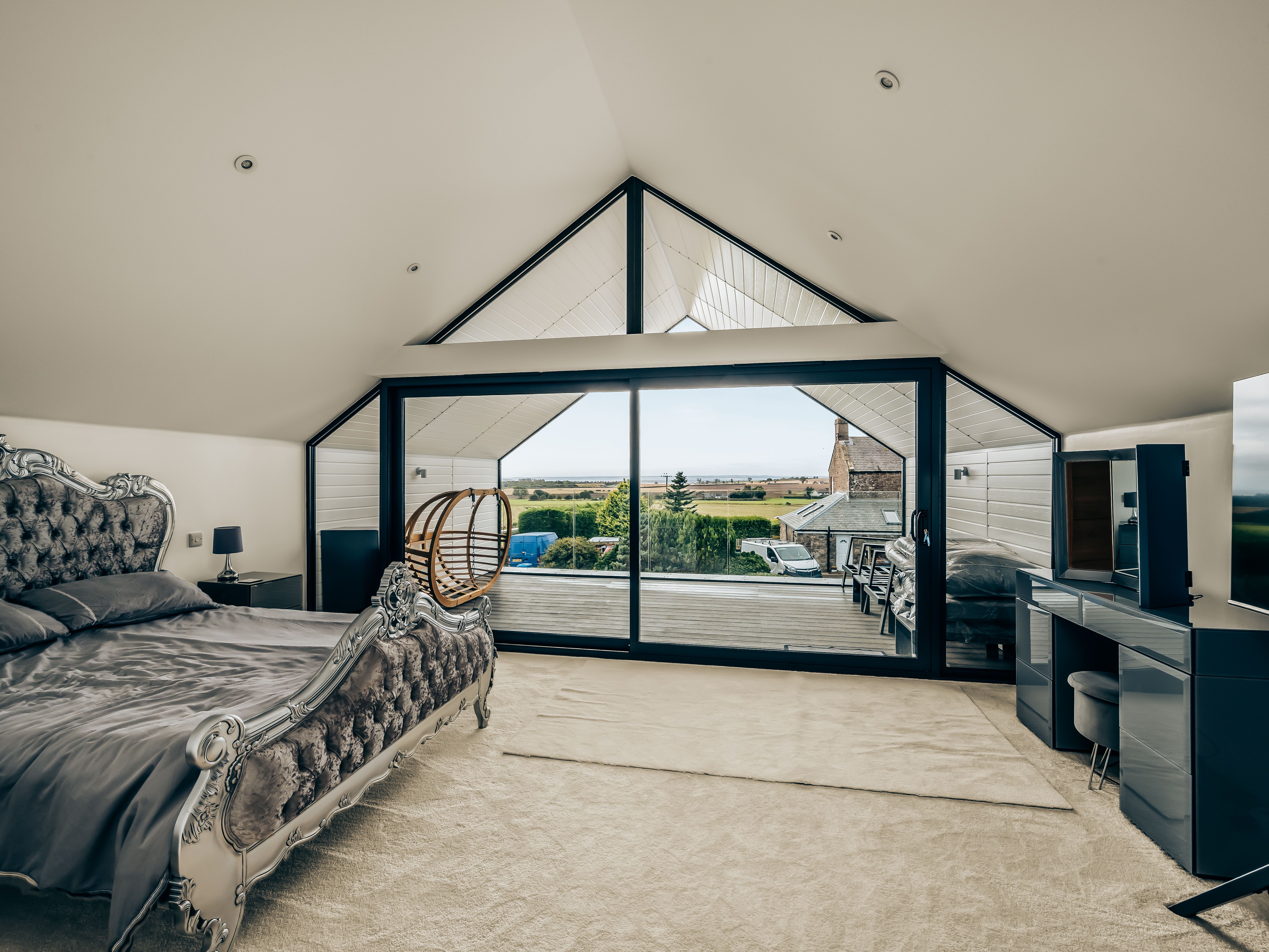 Modern loft bedroom with ornate bed, large glass doors, and a scenic outdoor view