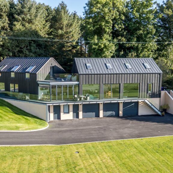 Modern black metal and glass house with large windows, surrounded by green lawns and trees.