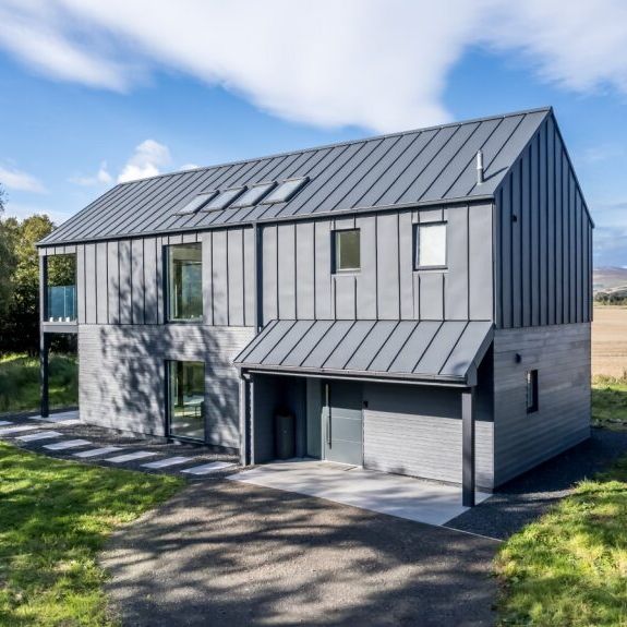 Modern two-story gray house with metal roof in a rural landscape