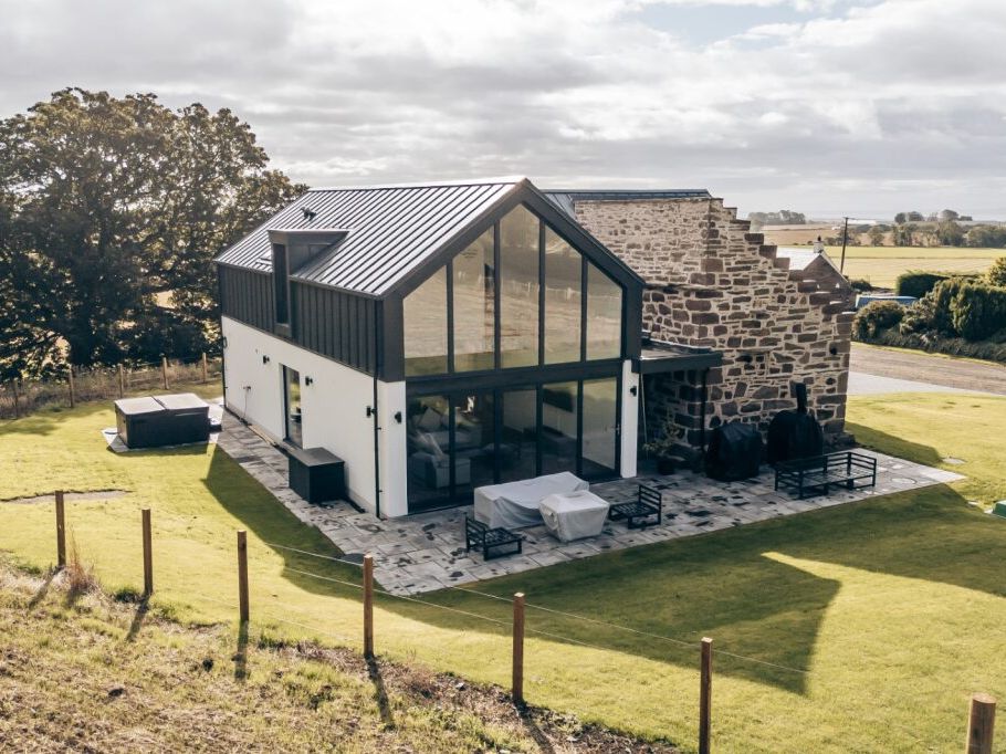 Modern farmhouse with large glass windows and stone wall exterior surrounded by green fields