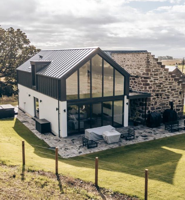 Modern farmhouse with large glass windows and stone wall exterior surrounded by green fields