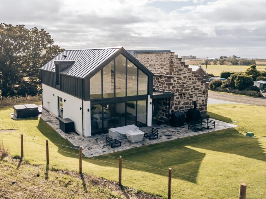 Modern farmhouse with large glass windows and stone wall exterior surrounded by green fields