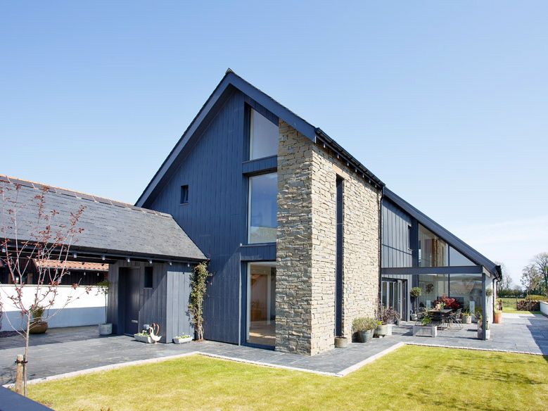Modern house with stone and dark wood exterior, large windows, and sloped roof