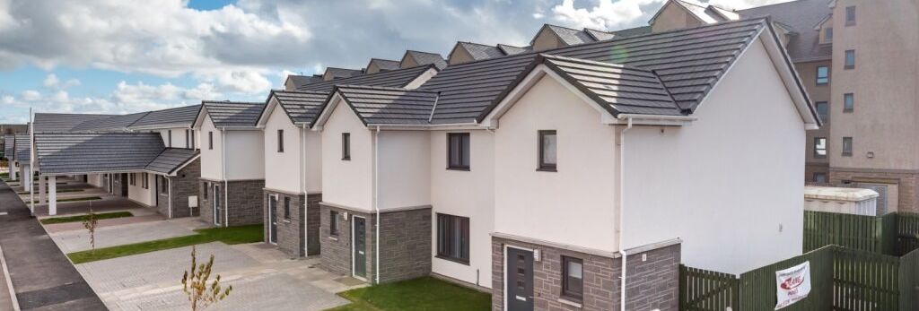 Row of modern semi-detached houses with driveways on a residential street under a blue sky with clouds.