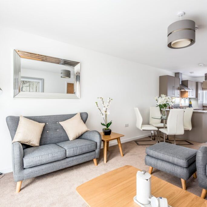 Modern open-plan living room and kitchen with grey sofas, dining table, and large mirror