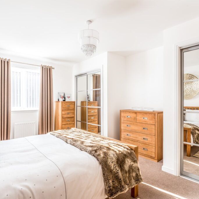 Bright modern bedroom with white walls, wooden furniture, and mirrored closet doors