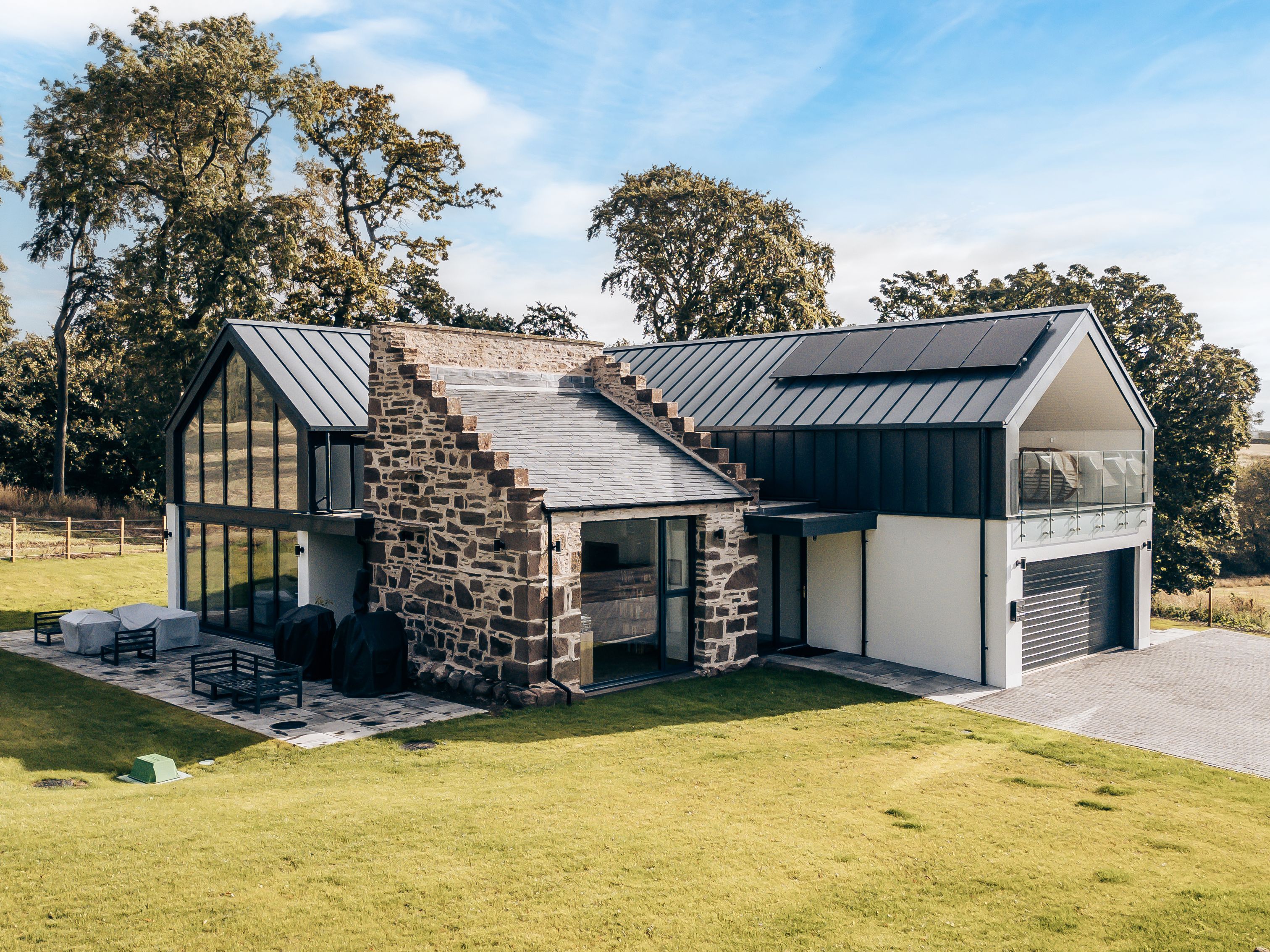 Modern house with stone and glass exterior surrounded by green lawn and trees.
