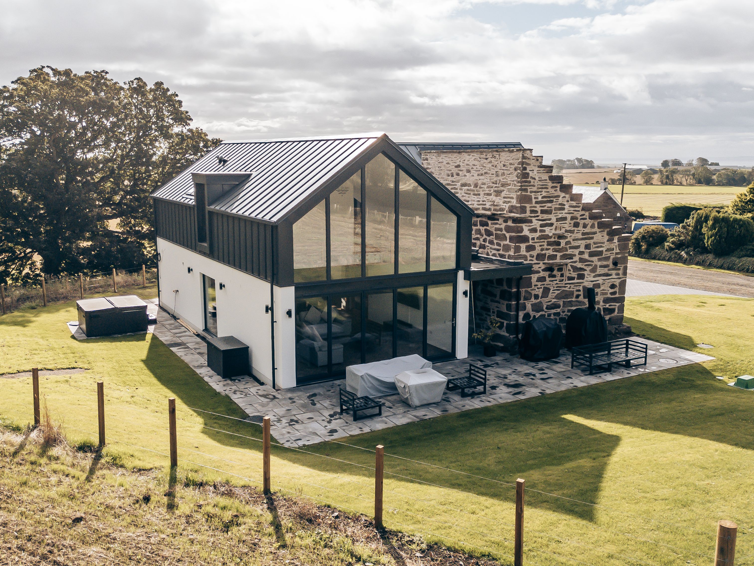 Modern house with large glass windows and stone wall in a rural landscape