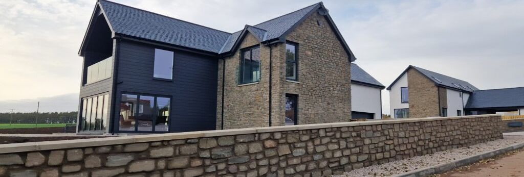 Modern houses with stone walls and large windows behind a stone fence