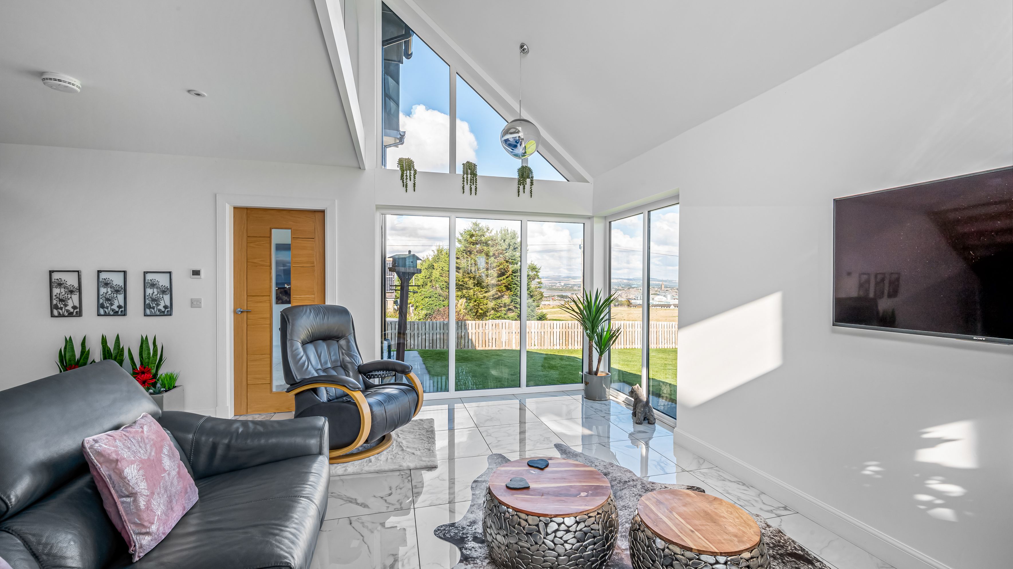 Modern living room with large windows, leather furniture, and view of backyard.