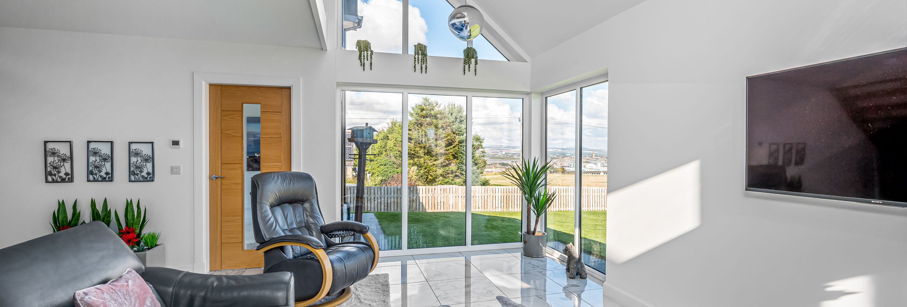 Modern living room with large windows, leather furniture, and view of backyard.