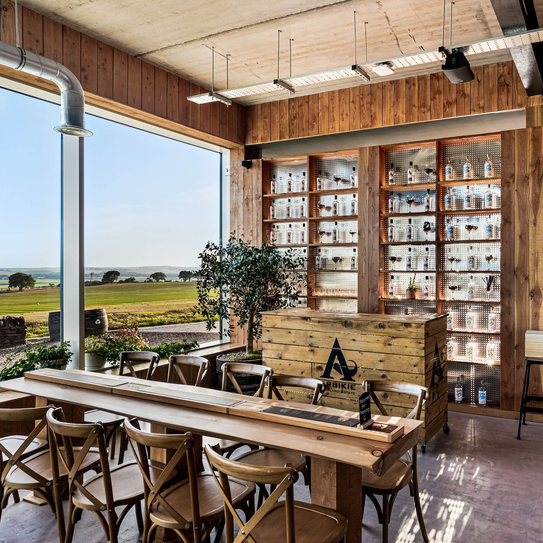 Modern distillery tasting room with wooden decor, shelves of bottles, and countryside view