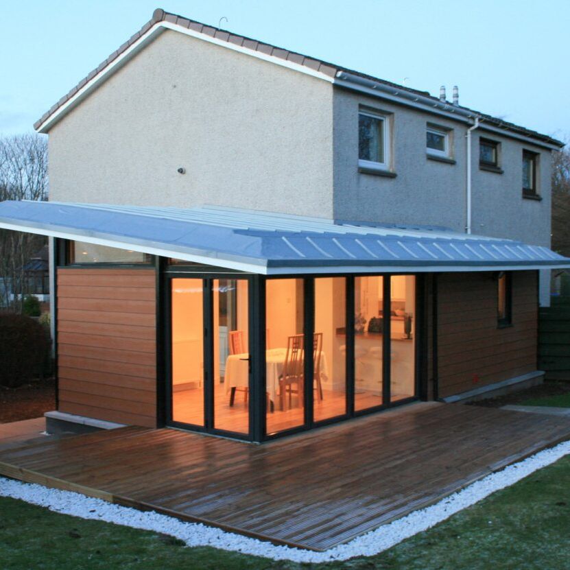 Modern house extension with wooden cladding, large glass sliding doors, and a patio deck