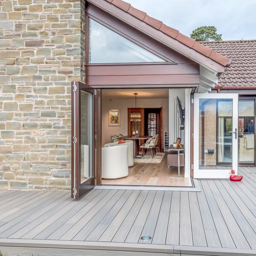 Modern house with stone wall, open patio doors, and view into a stylish living and dining area