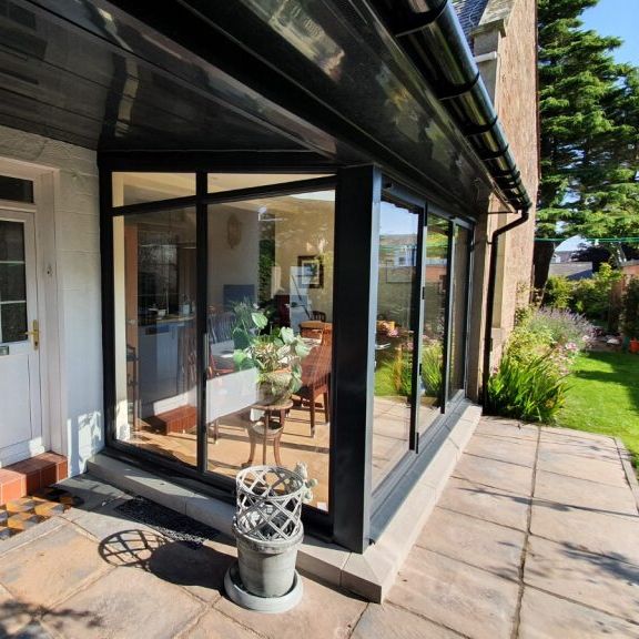 Modern glass sunroom extension attached to a house, with a view of the garden and outdoor patio.