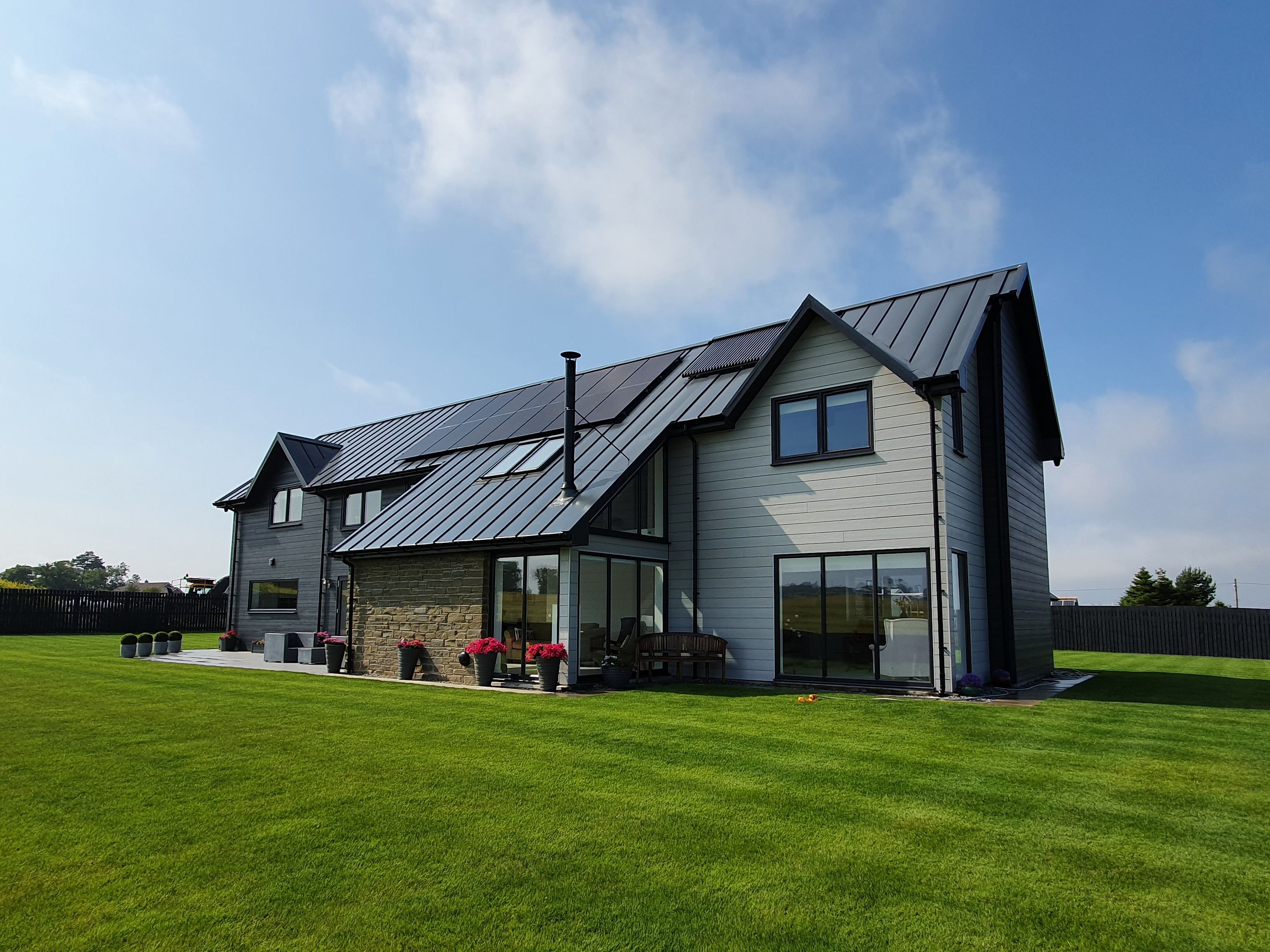 Modern two-story house with large windows and a metal roof, surrounded by a well-manicured lawn