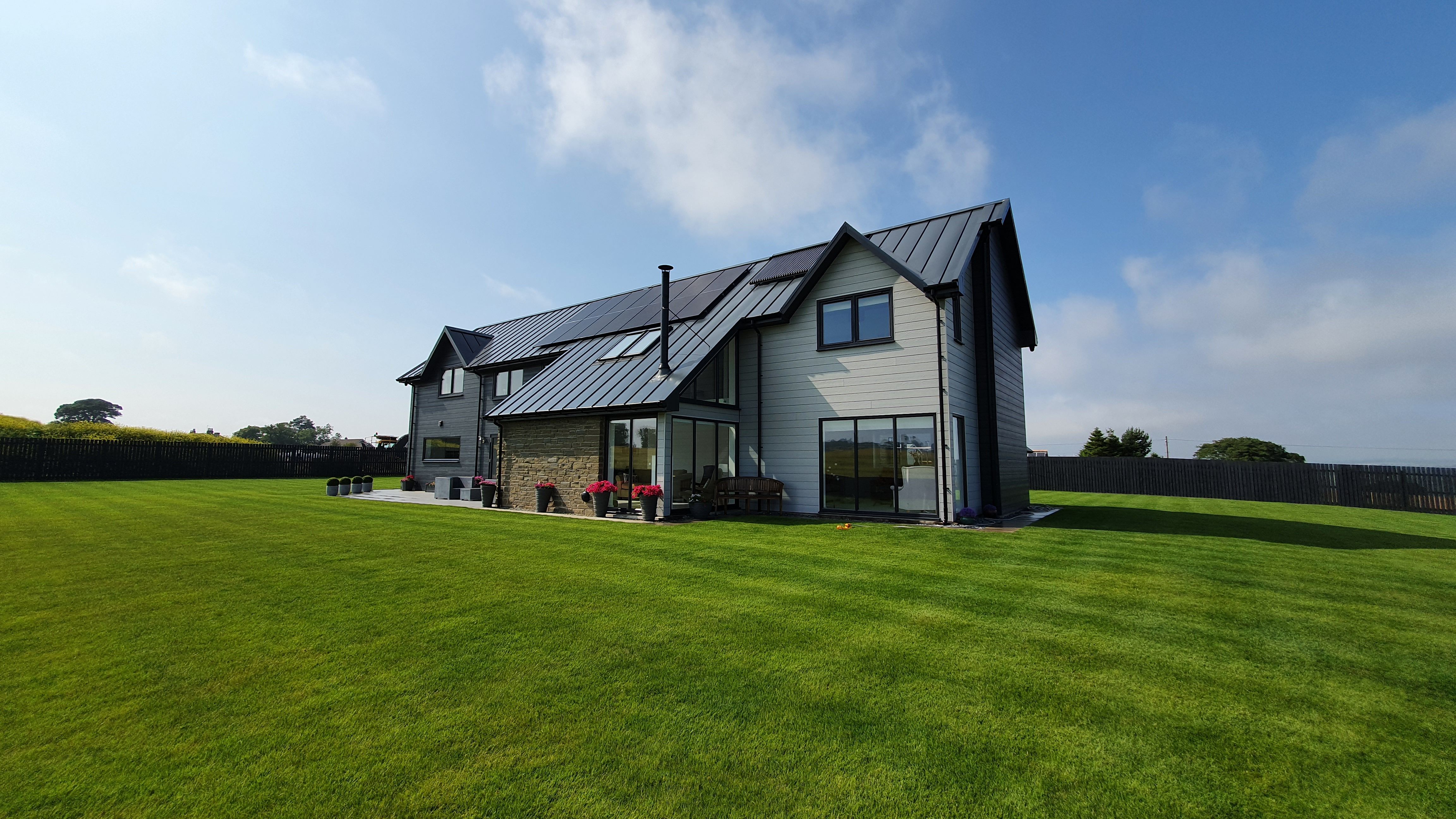 Modern two-story house with large windows and a metal roof, surrounded by a well-manicured lawn