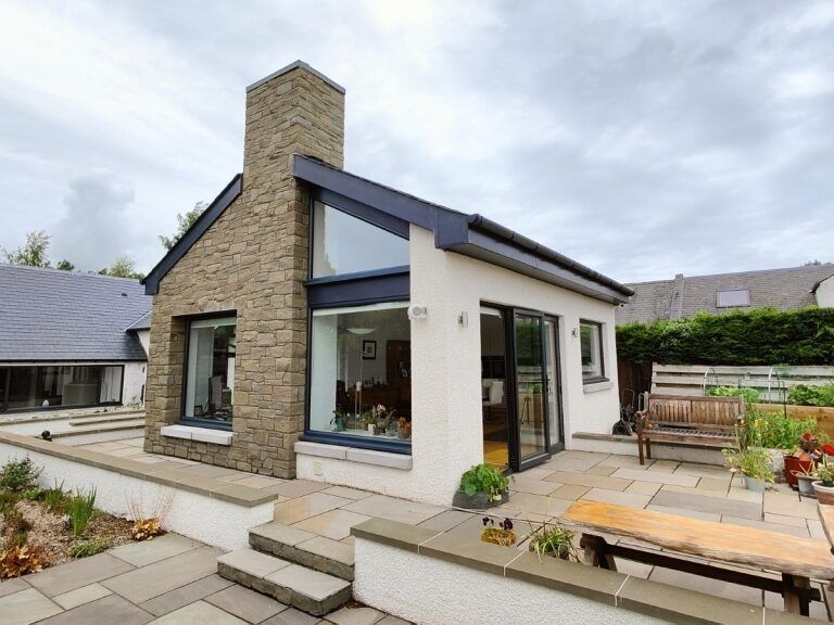 Modern house extension with stone chimney, large glass windows, and patio garden