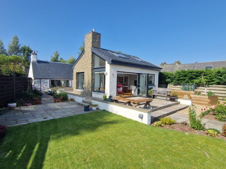 Modern house with a patio, garden, and lawn on a sunny day
