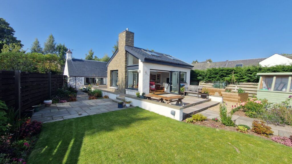 Modern house with a patio, garden, and lawn on a sunny day