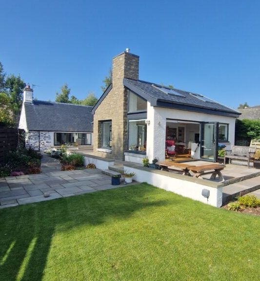 Modern house with a patio, garden, and lawn on a sunny day