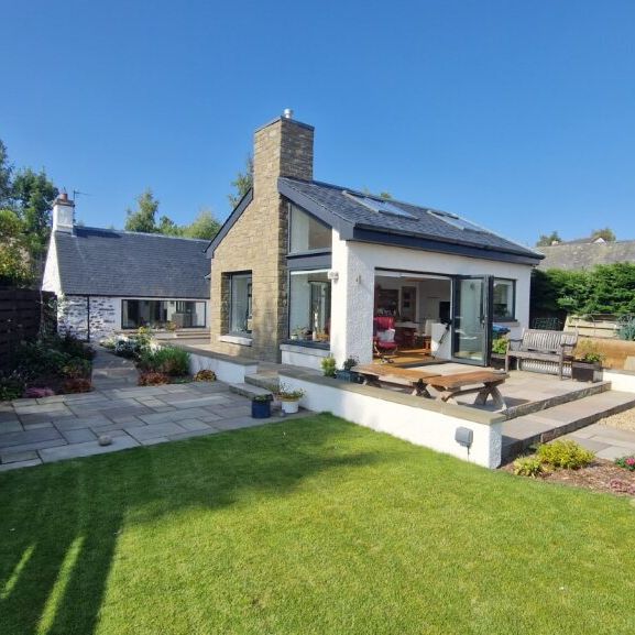 Modern house with a patio, garden, and lawn on a sunny day